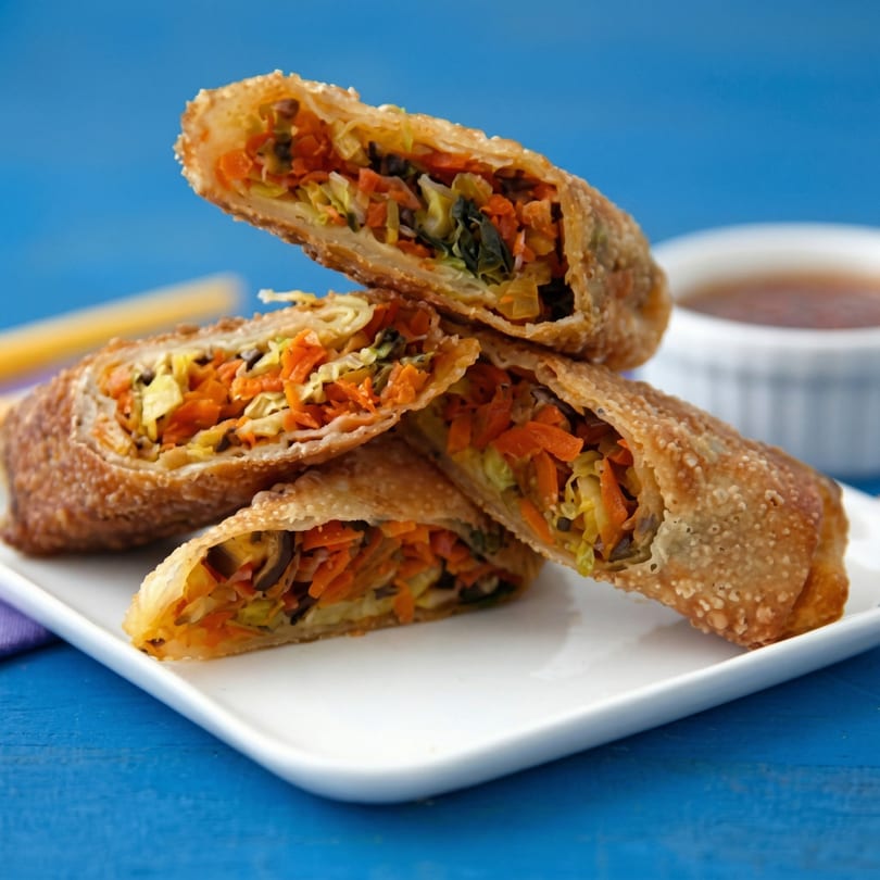 Crispy egg rolls, cut in half, revealing a colorful vegetable filling, with dipping sauce.