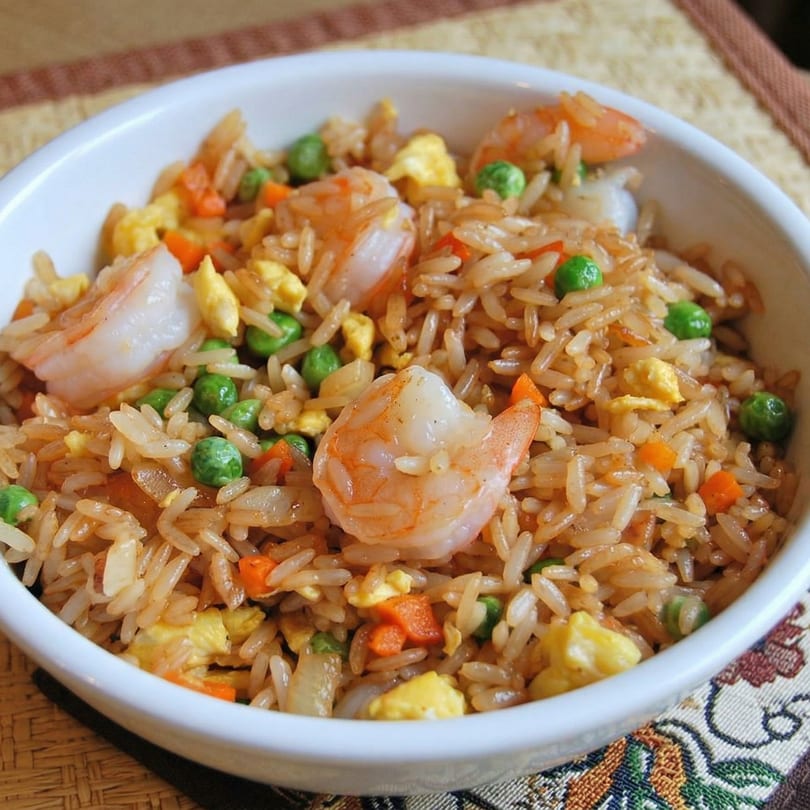 Shrimp fried rice with peas, carrots, and scrambled egg in a white bowl.